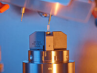 Close-up of a Satisloh SPM-10 grinding machine processing micro rod lenses in precision optics.