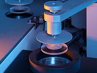Close-up of a precision machine handling an optical lens during manufacturing.