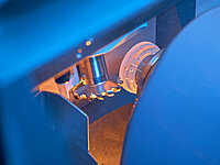 Close-up of an industrial machine processing a glass lens with a rotating tool