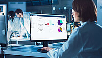 Scientist analyzing data on a computer screen displaying charts and graphs in a laboratory.
