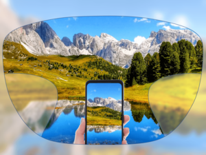 View through a pair of glasses showing a clear landscape with mountains, trees, and a lake, with a smartphone held in the center capturing the same scene.