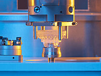 Precision machine tool processing an optical lens under controlled lighting.