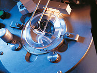 Close-up of a glass lens being precisely processed in a machine with fine tools
