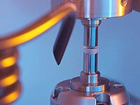 Close-up of laboratory tool holding a small cylindrical sample for precision testing
