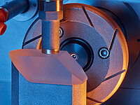 Close-up of a Satisloh PR-150 grinding machine processing prisms in precision optics manufacturing.