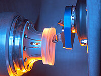 Close-up of a machine processing a glass lens between two precision tools.