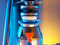 Close-up of an industrial machine holding and processing a glass lens with precision tools.