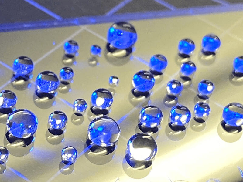 Close-up of water droplets on a semiconductor wafer surface reflecting blue light.