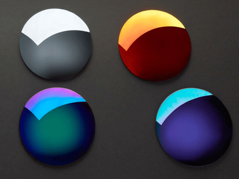 Four semiconductor wafers in different reflective colors including white, red, green, and blue, placed on a dark background.