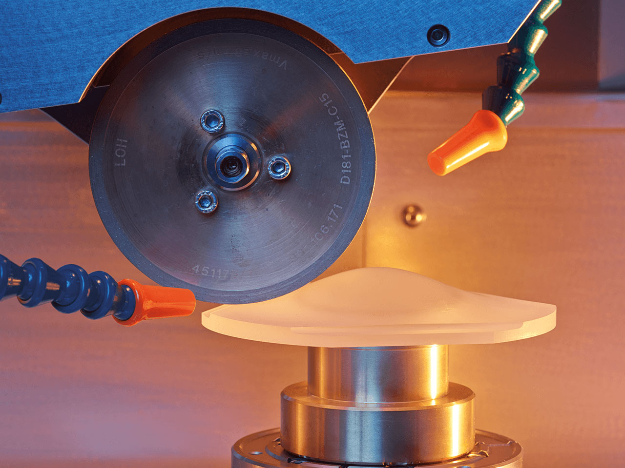 Close-up of a Satisloh precision optics grinding machine processing a lens.